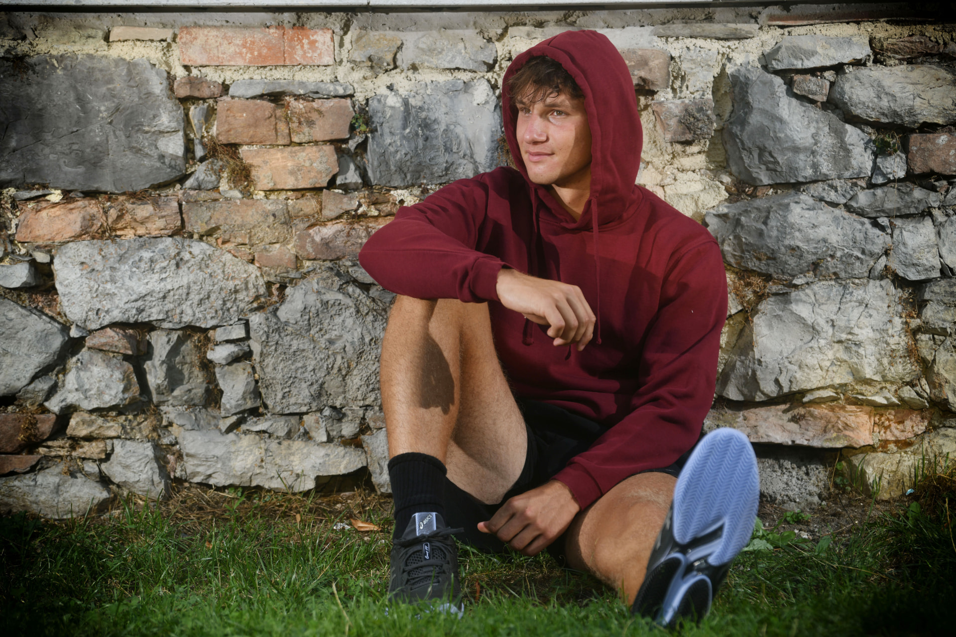 Gil Kita in a red hoodie beside a stone wall